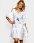 Woman wearing a white dress with blue patterns and a blue tassel against a plain background