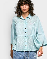 Woman wearing a light blue polka dot shirt against a plain background