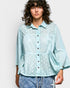 Woman wearing a light blue polka dot shirt against a plain background