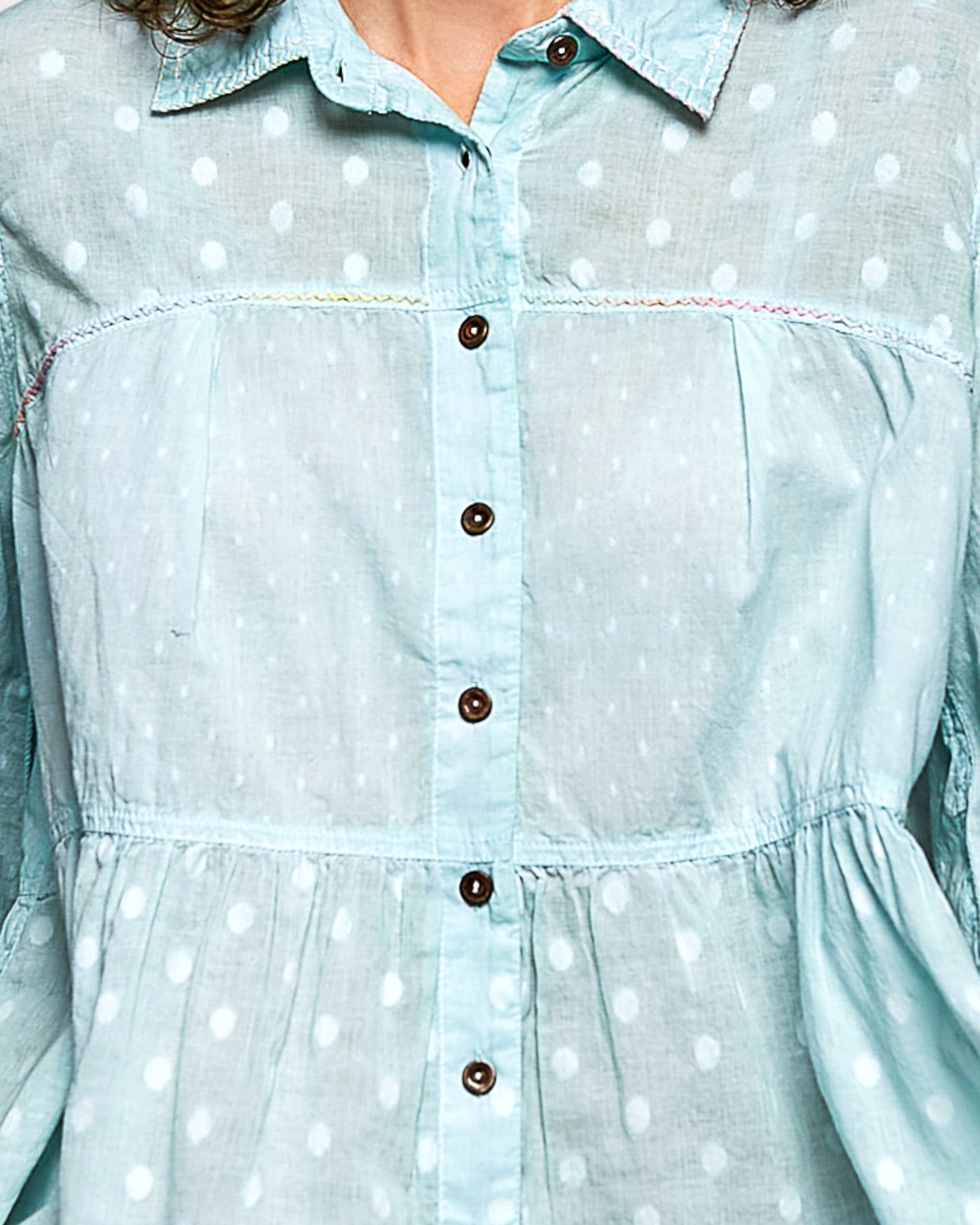 Light blue blouse with polka dots and brown buttons on a blurred background