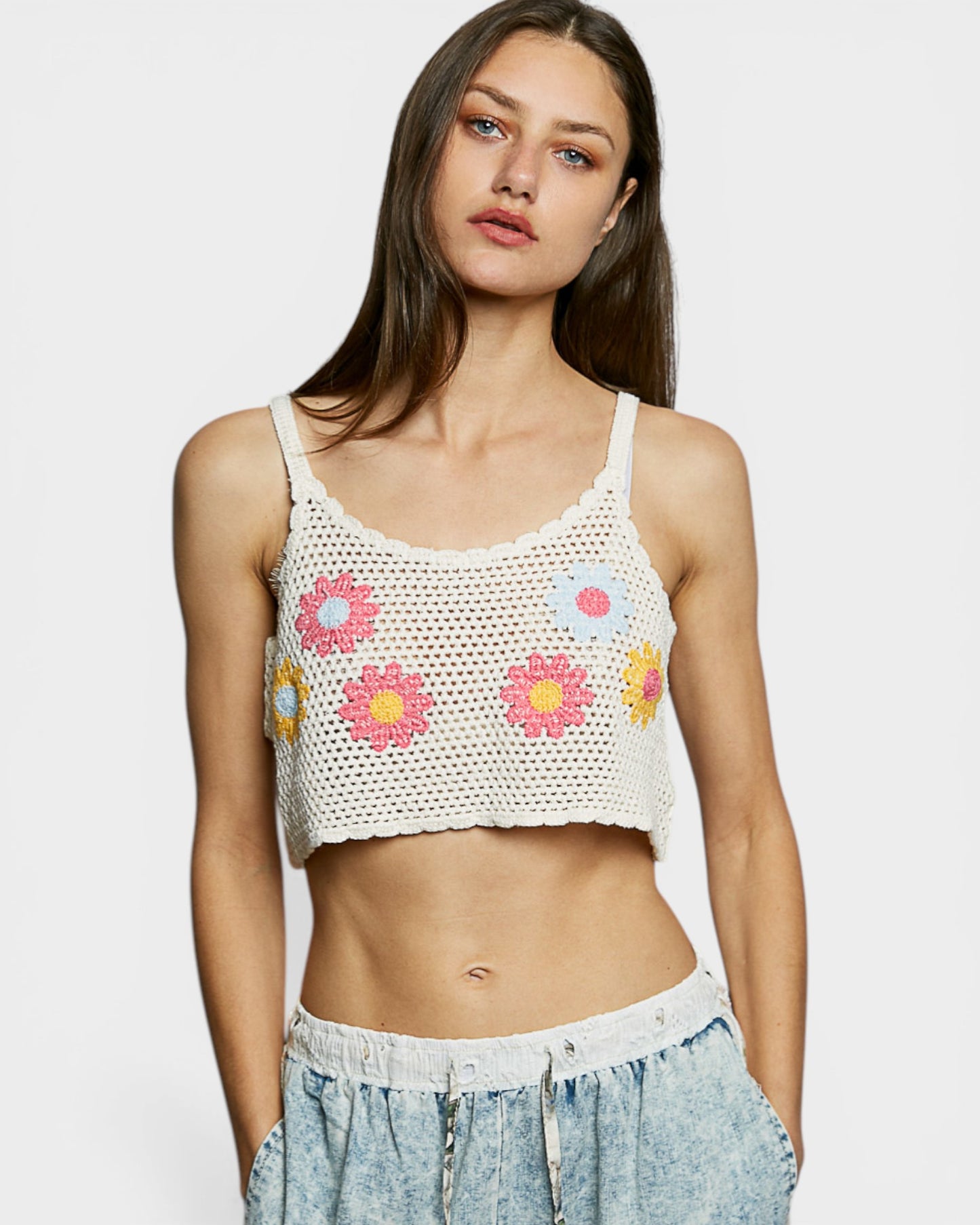 Woman wearing a crochet tank top with floral patterns on a plain background