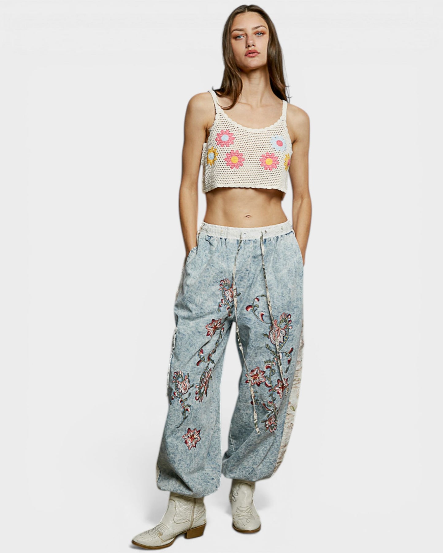 Woman wearing a floral tank top and embroidered denim pants on a white background