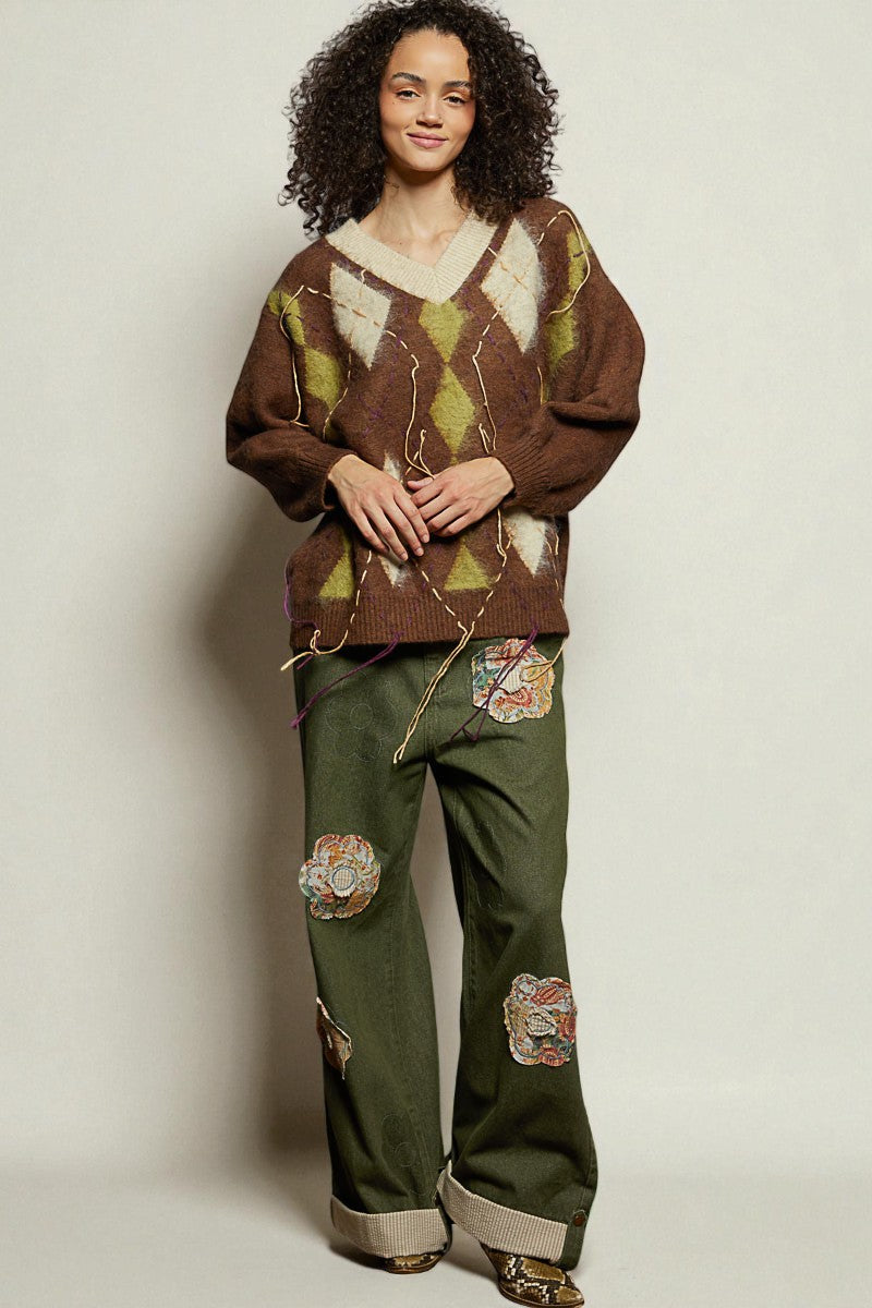 Woman wearing a patterned sweater and green pants with patches on a plain background