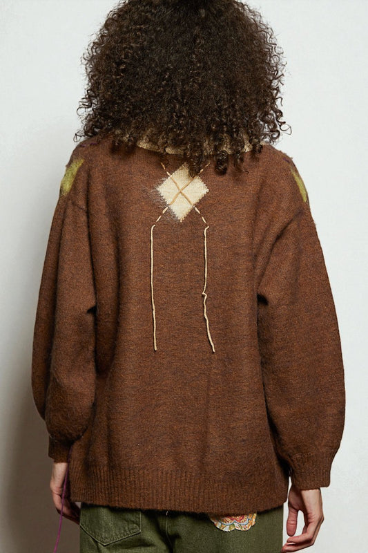 Person wearing a brown sweater with a geometric pattern on the back against a plain background