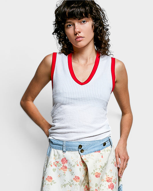 Woman wearing a white tank top with red trim and floral skirt on a plain background