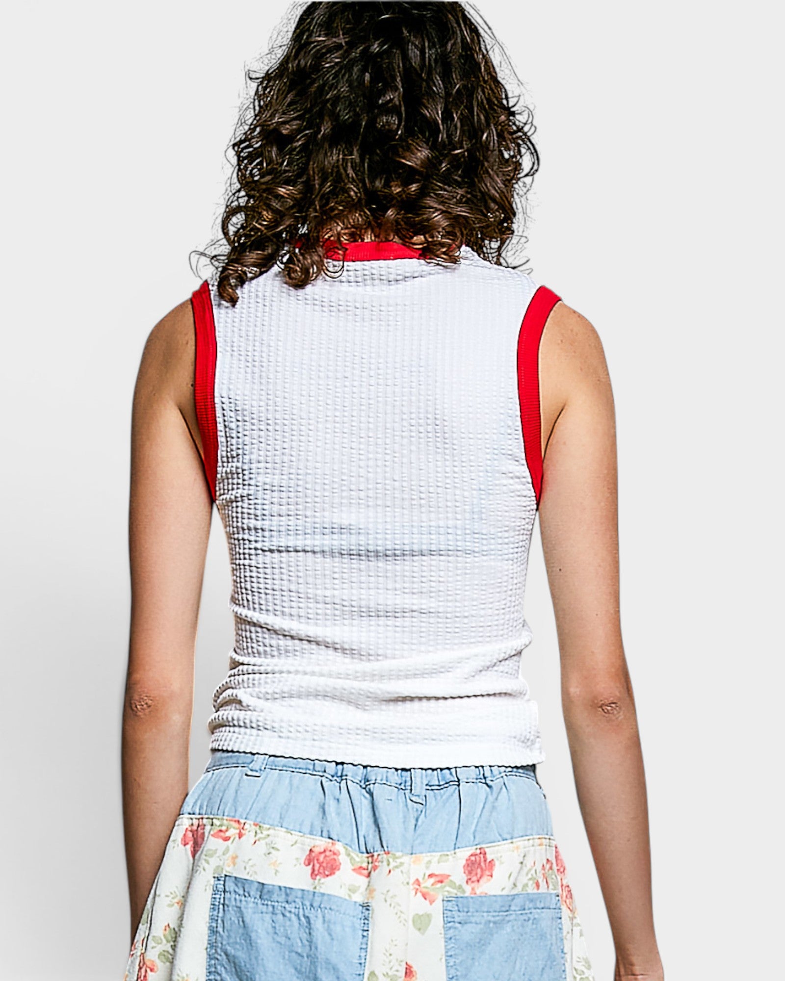 Person wearing a white sleeveless top with red straps on a plain background
