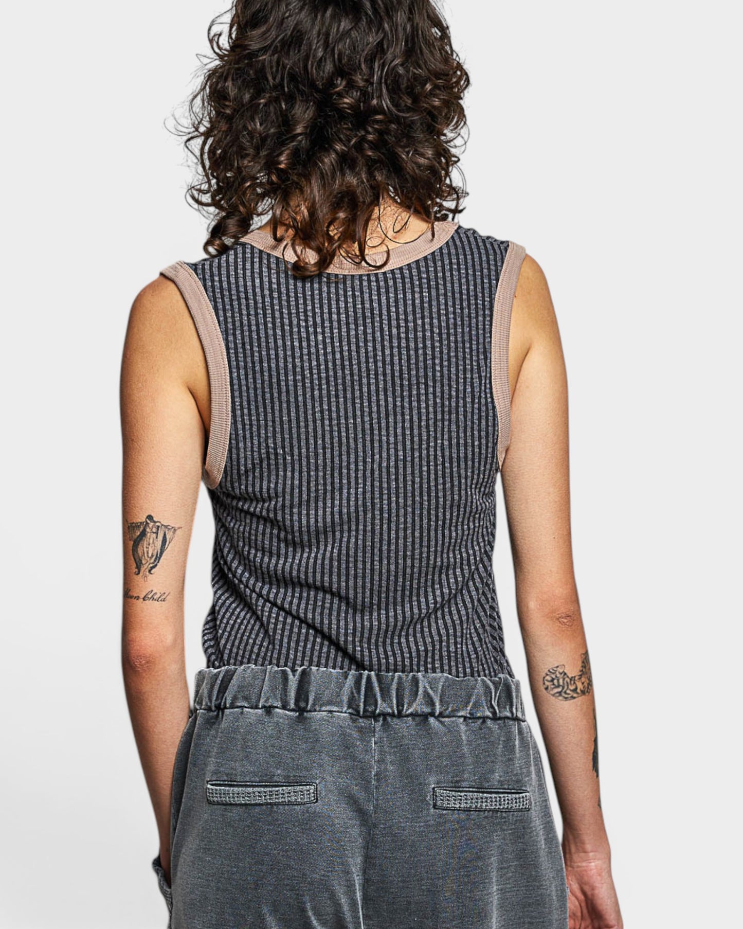 Person wearing a sleeveless, patterned top and gray pants on a plain background