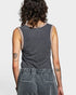Person wearing a sleeveless, patterned top and gray pants on a plain background