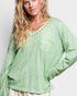 Woman wearing a green long-sleeve top with decorative trim on a plain background