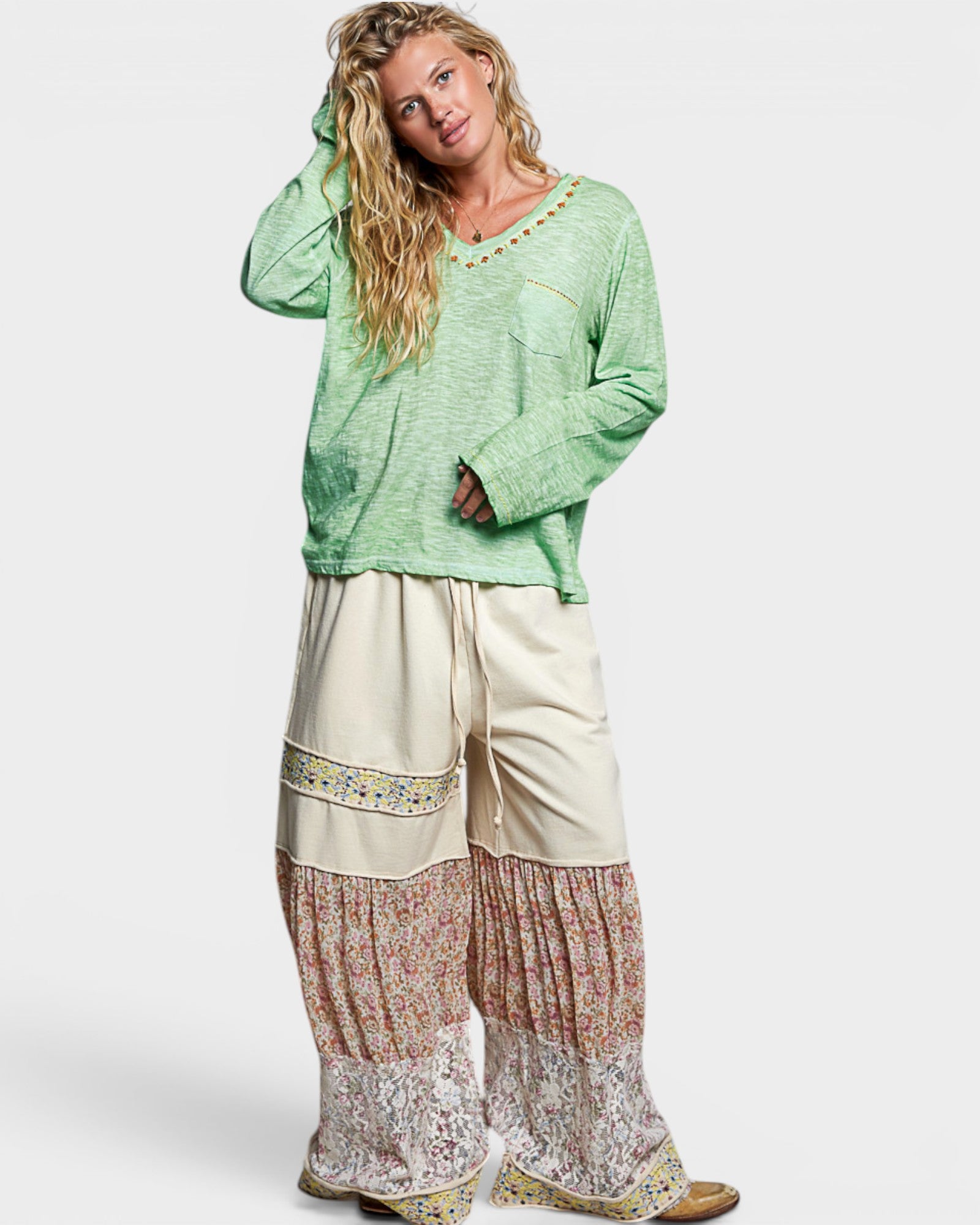 Woman wearing a green top and patterned beige pants on a white background