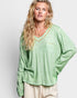 Woman wearing a green long-sleeve top with decorative trim on a white background