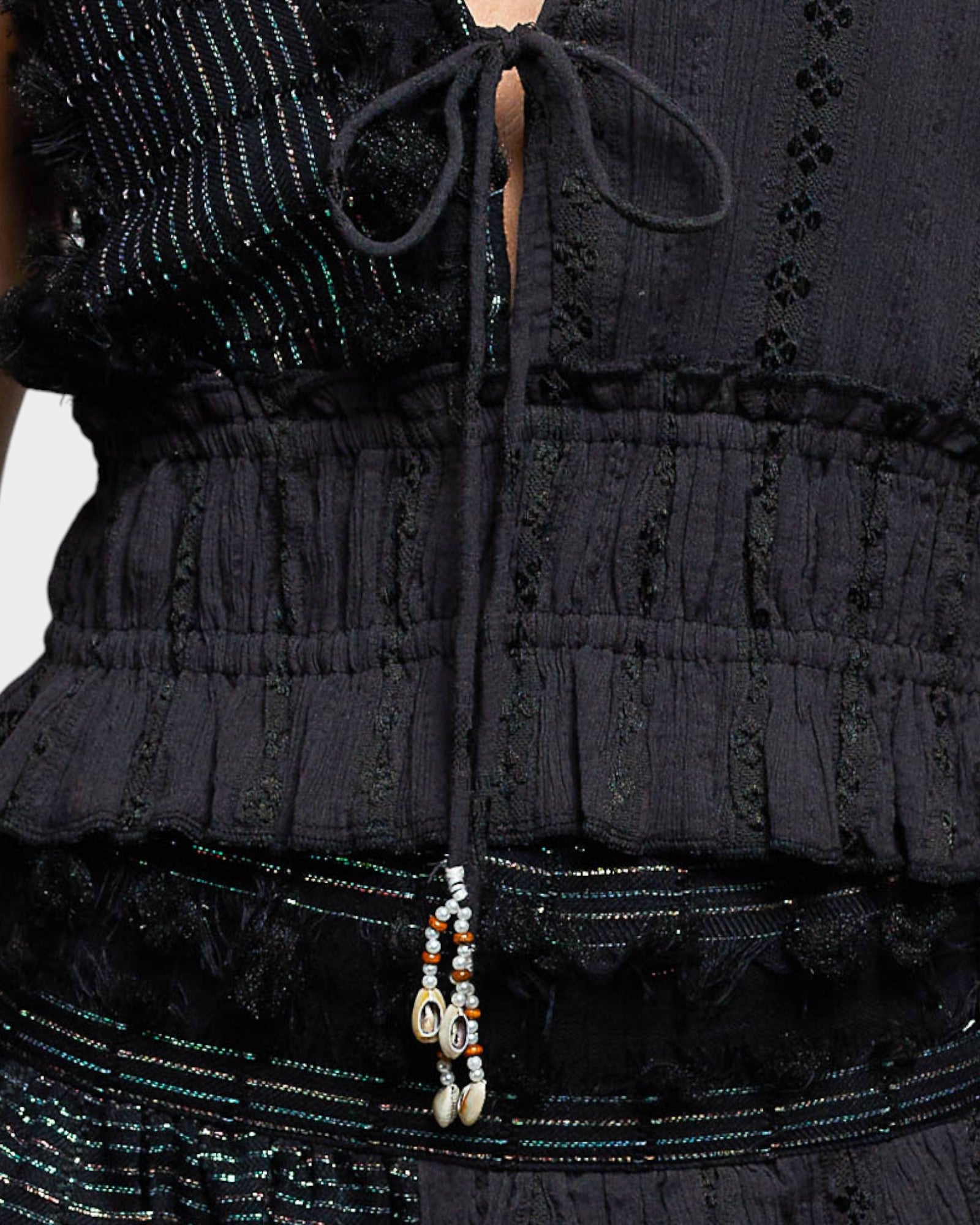 Close-up of a black textured top with a beaded detail on a white background