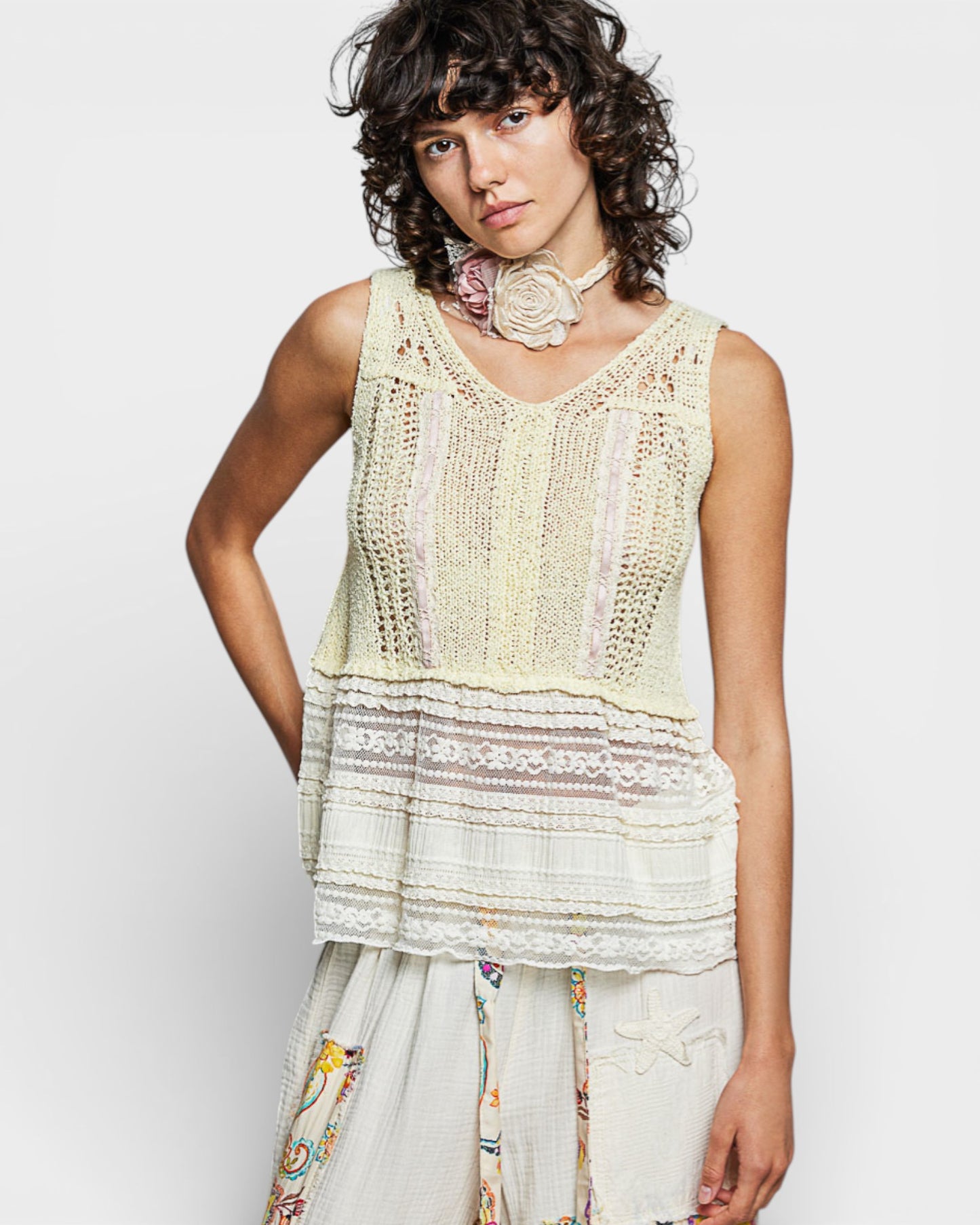 Woman wearing a light green crochet top and floral pants on a white background