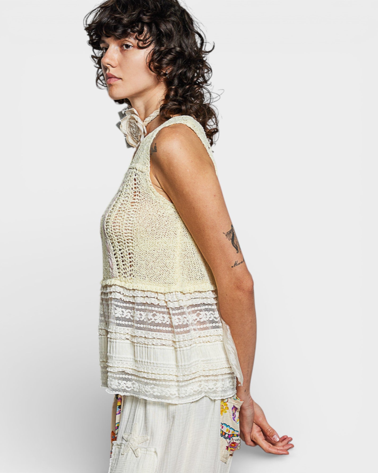 Woman wearing a light-colored crochet top with a plain background