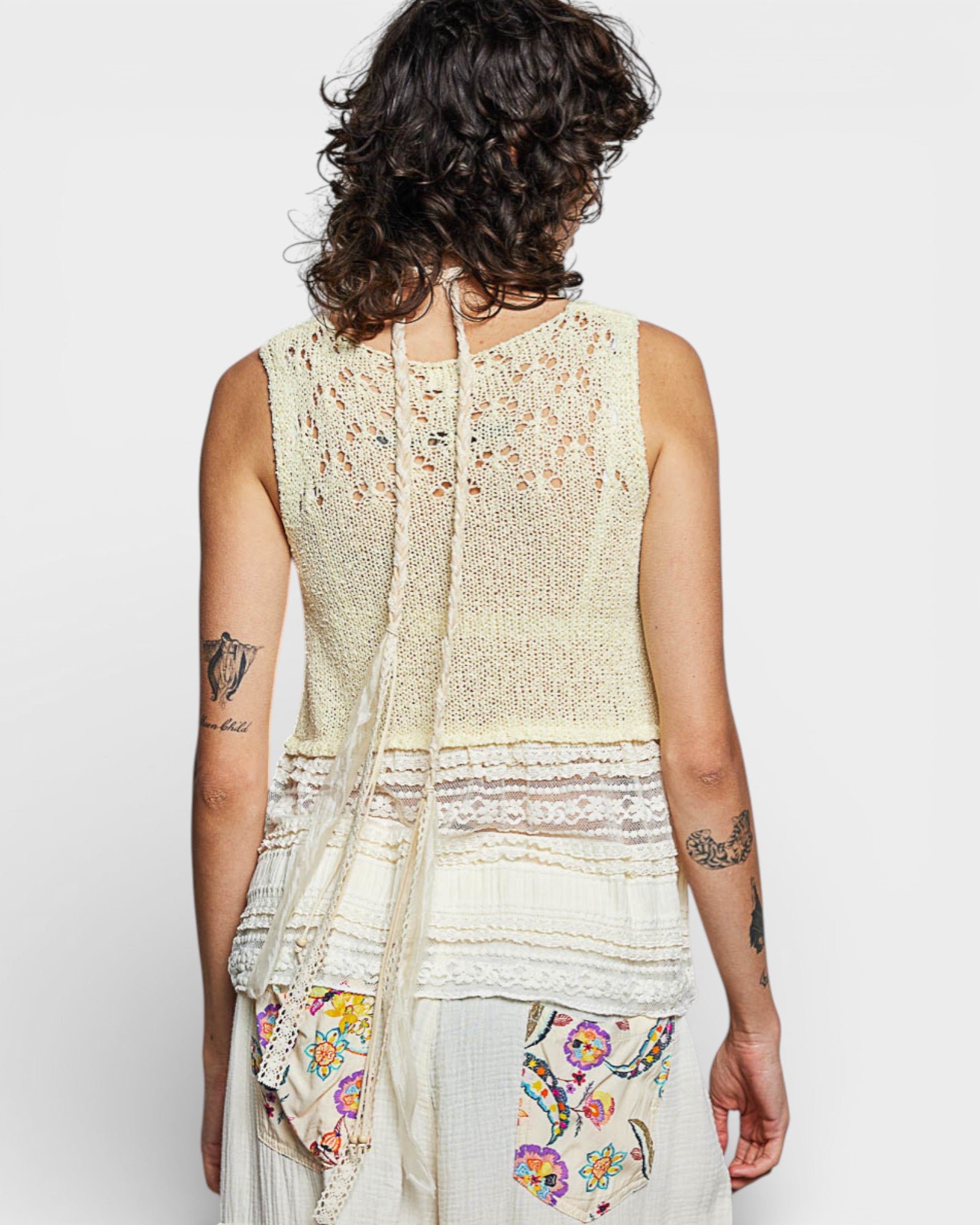 Person wearing a light-colored sleeveless top with a floral scarf, on a plain background