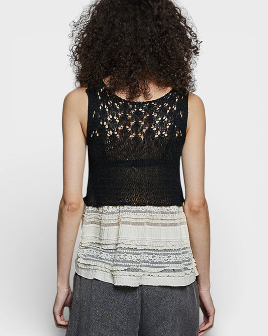 Person wearing a black lace top with a white lace trim over a gray skirt on a white background