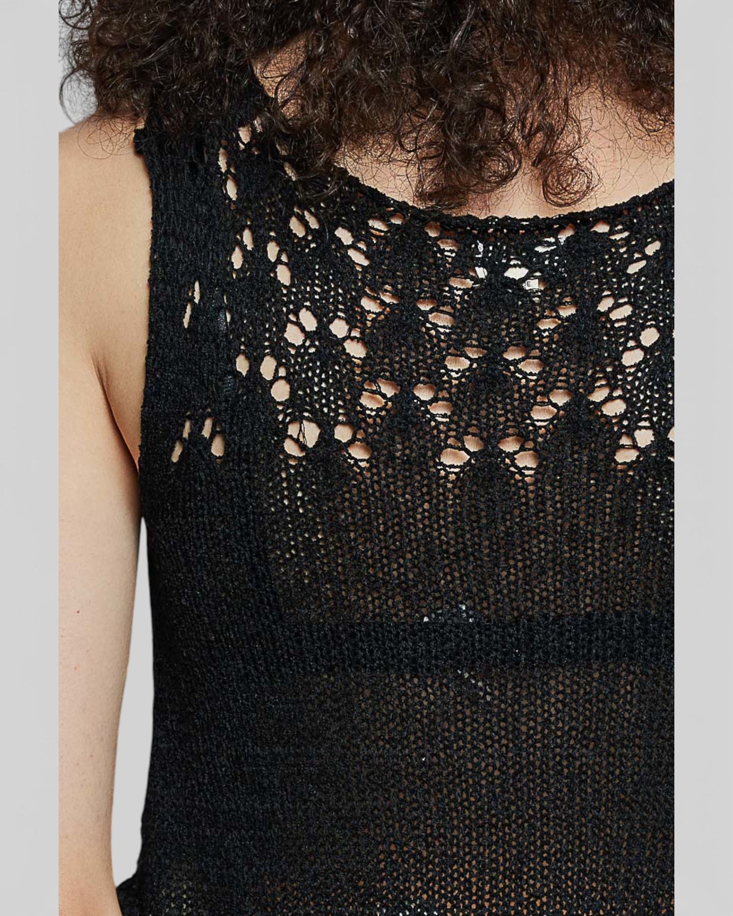 Black sleeveless top with intricate lace detailing on a plain background