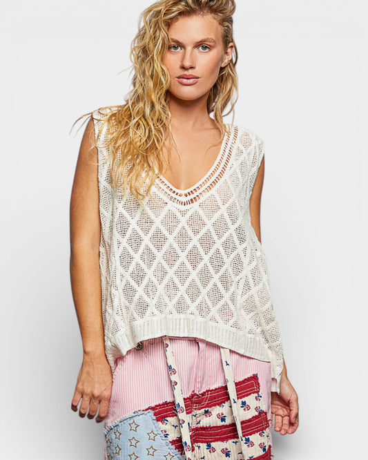 Woman wearing a white crochet top with colorful pants on a light background