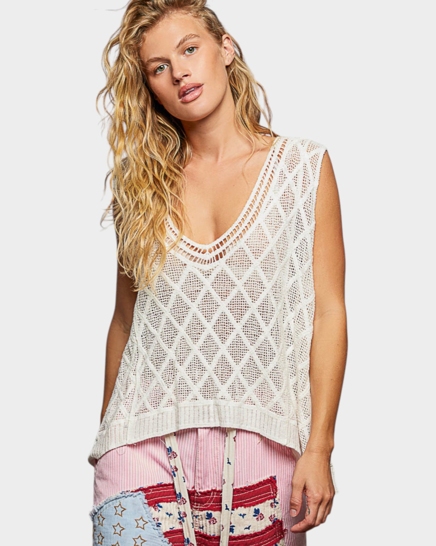 Woman wearing a white crochet tank top with colorful pants on a light background