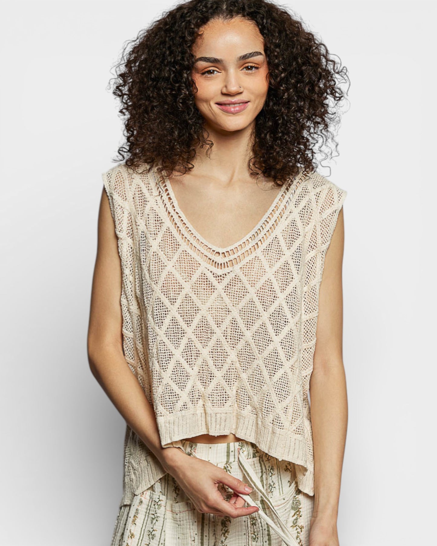 Woman wearing a beige crochet top against a plain background