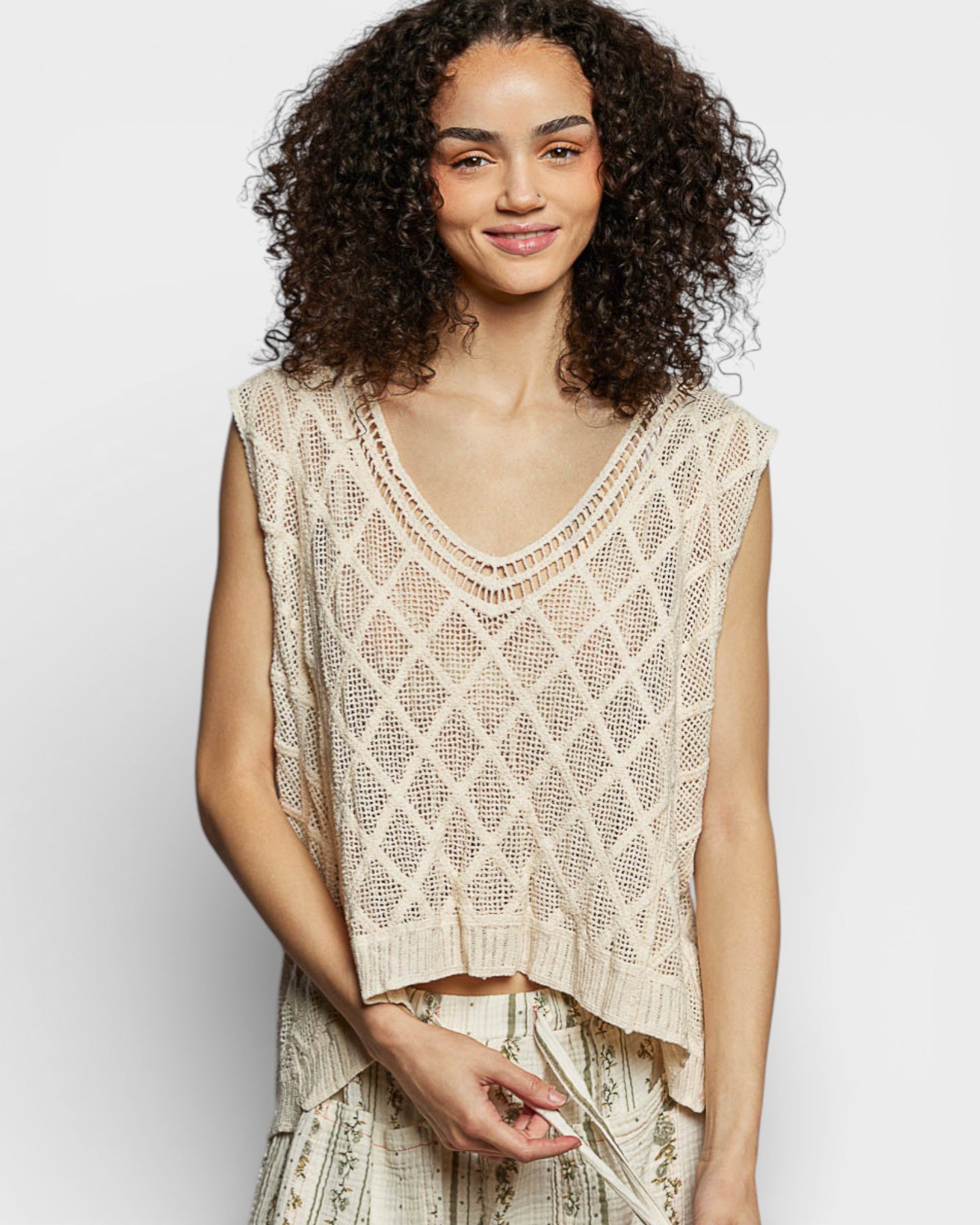 Woman wearing a beige crochet top against a plain background