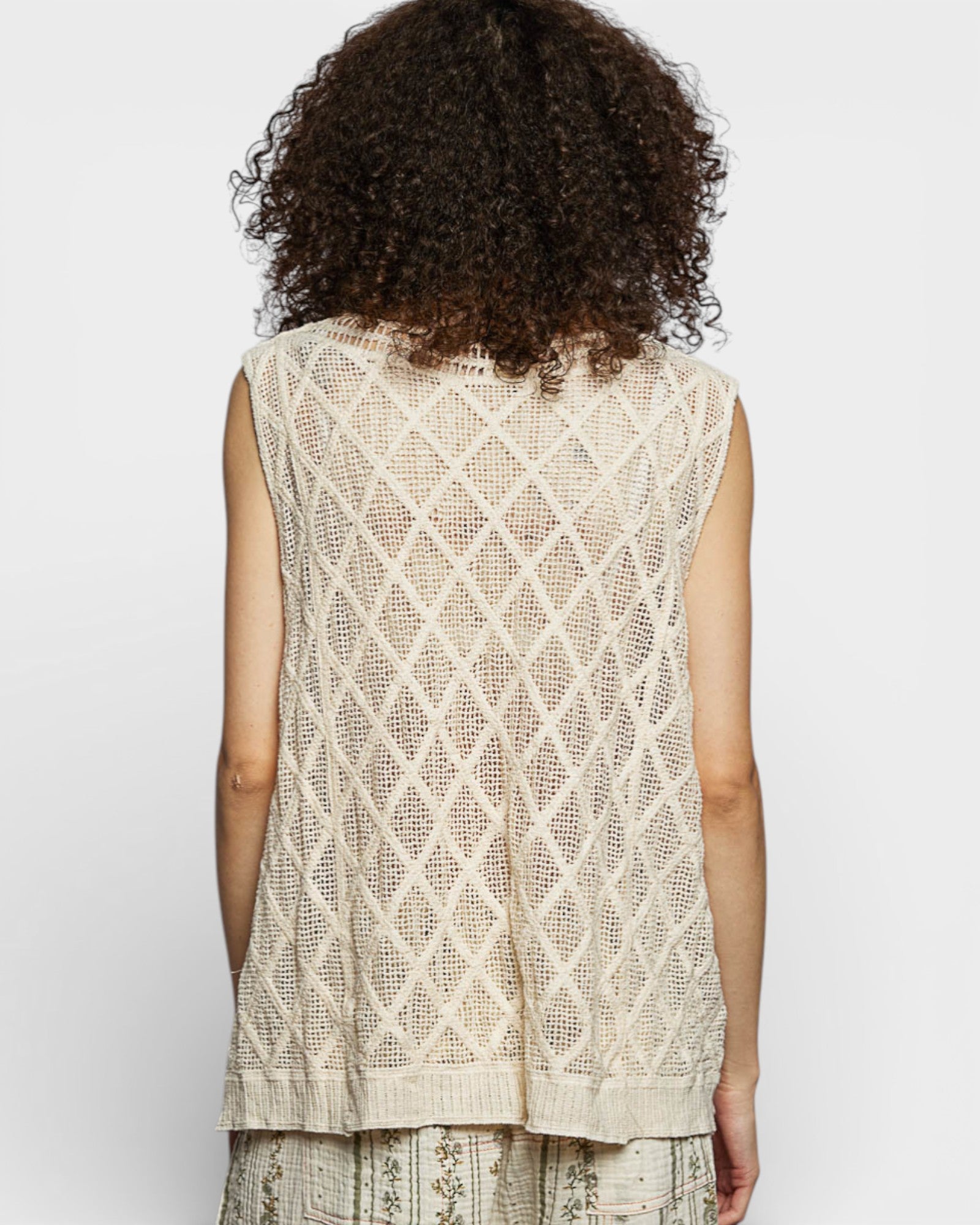 Woman wearing a beige sleeveless top with a diamond pattern on a white background