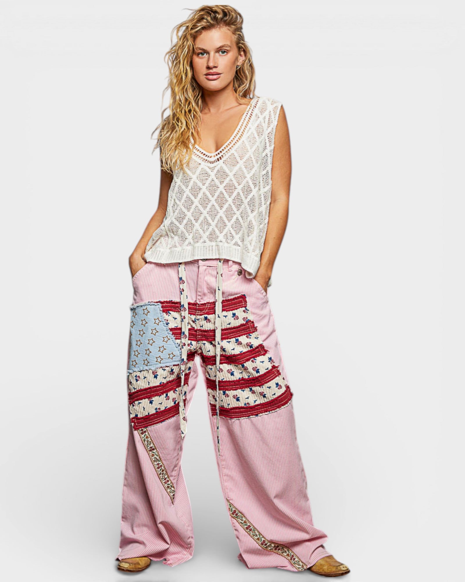 Woman wearing a sleeveless crochet top and pink pants with patterned details on a white background