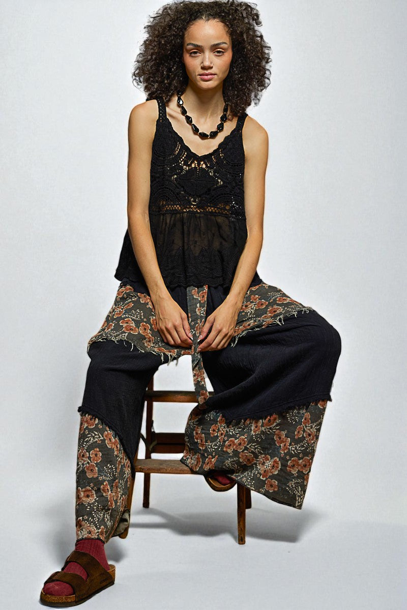 Woman sitting on a chair wearing a black sleeveless top and floral pants with a plain background