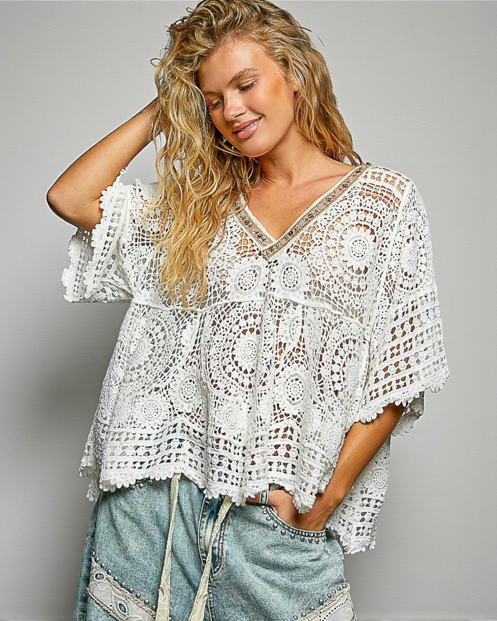 Woman wearing a white crochet top and denim shorts on a gray background