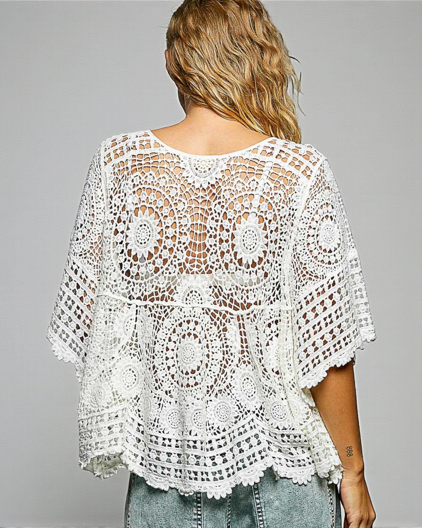 White crochet top worn by a person on a gray background