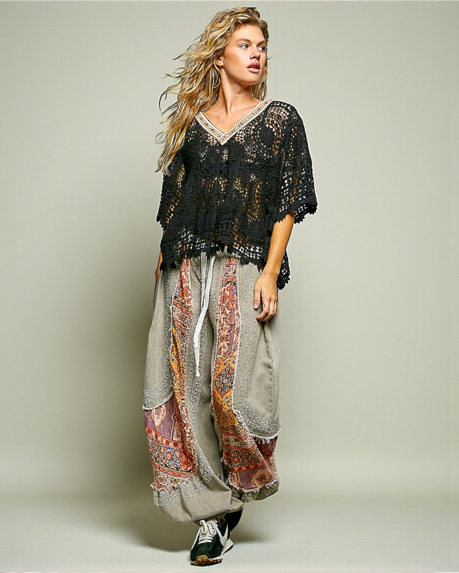 Woman wearing a black lace top and patterned harem pants on a plain background