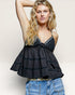 Woman wearing a black tiered top and blue jeans against a plain background