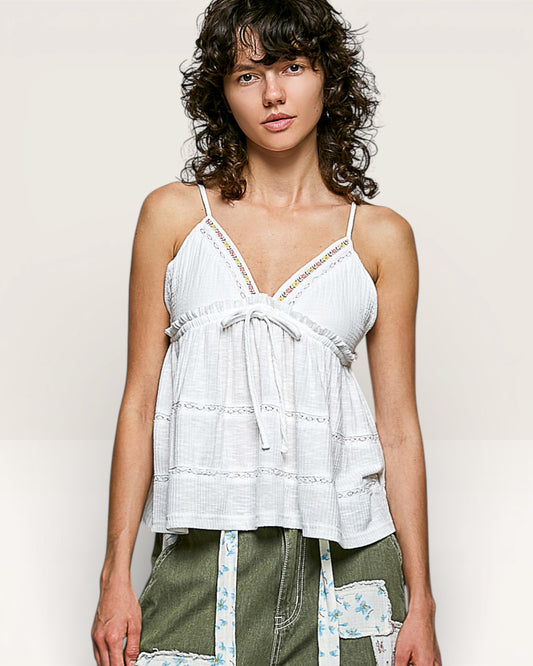 Woman wearing a white lace top with green pants against a plain background