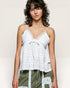 Woman wearing a white lace top with green pants against a plain background