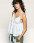 Woman wearing a white lace top with green pants against a plain background