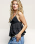 Woman wearing a black tiered top and blue jeans against a plain background