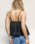 Woman wearing a black tiered tank top and blue jeans on a plain background
