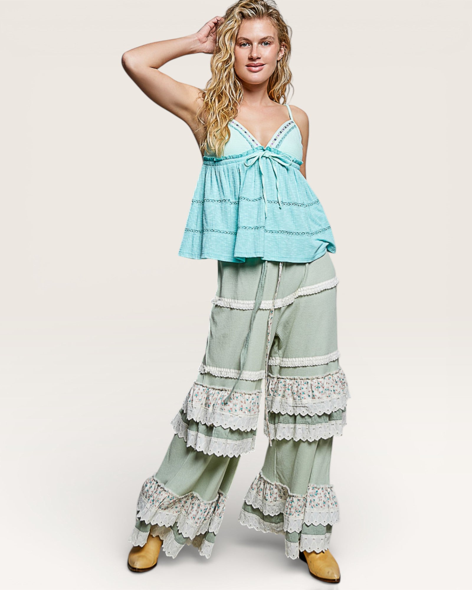 Woman wearing a light blue top and green pants with lace details on a white background