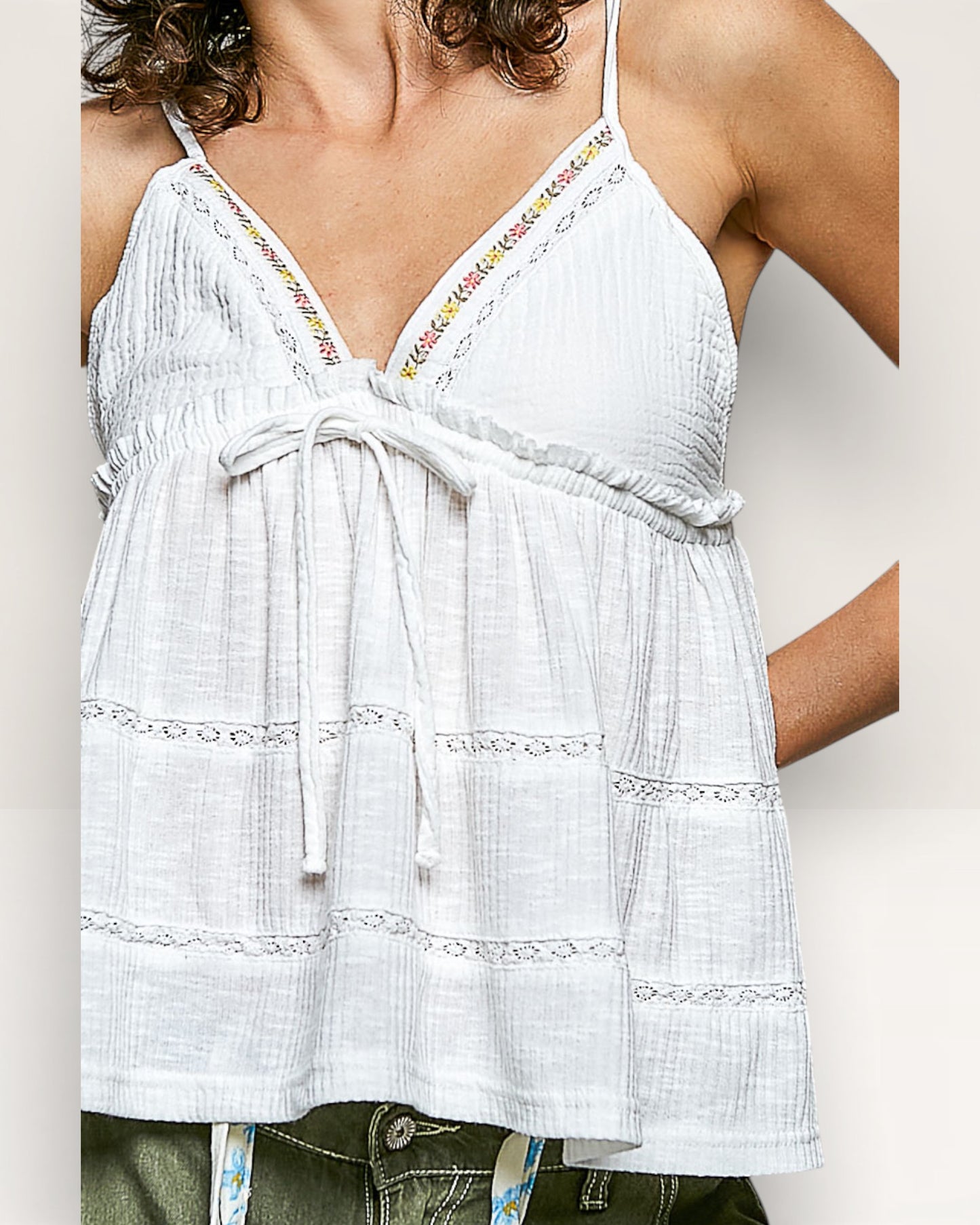 White sleeveless top with colorful embroidery on straps against a neutral background