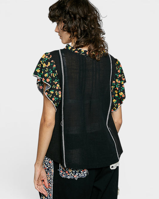 Woman wearing a black sleeveless top with floral embroidery on a white background