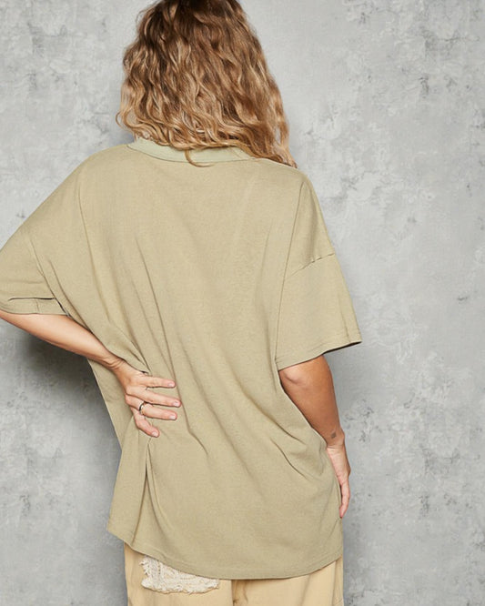 Person wearing a beige oversized shirt against a gray concrete wall