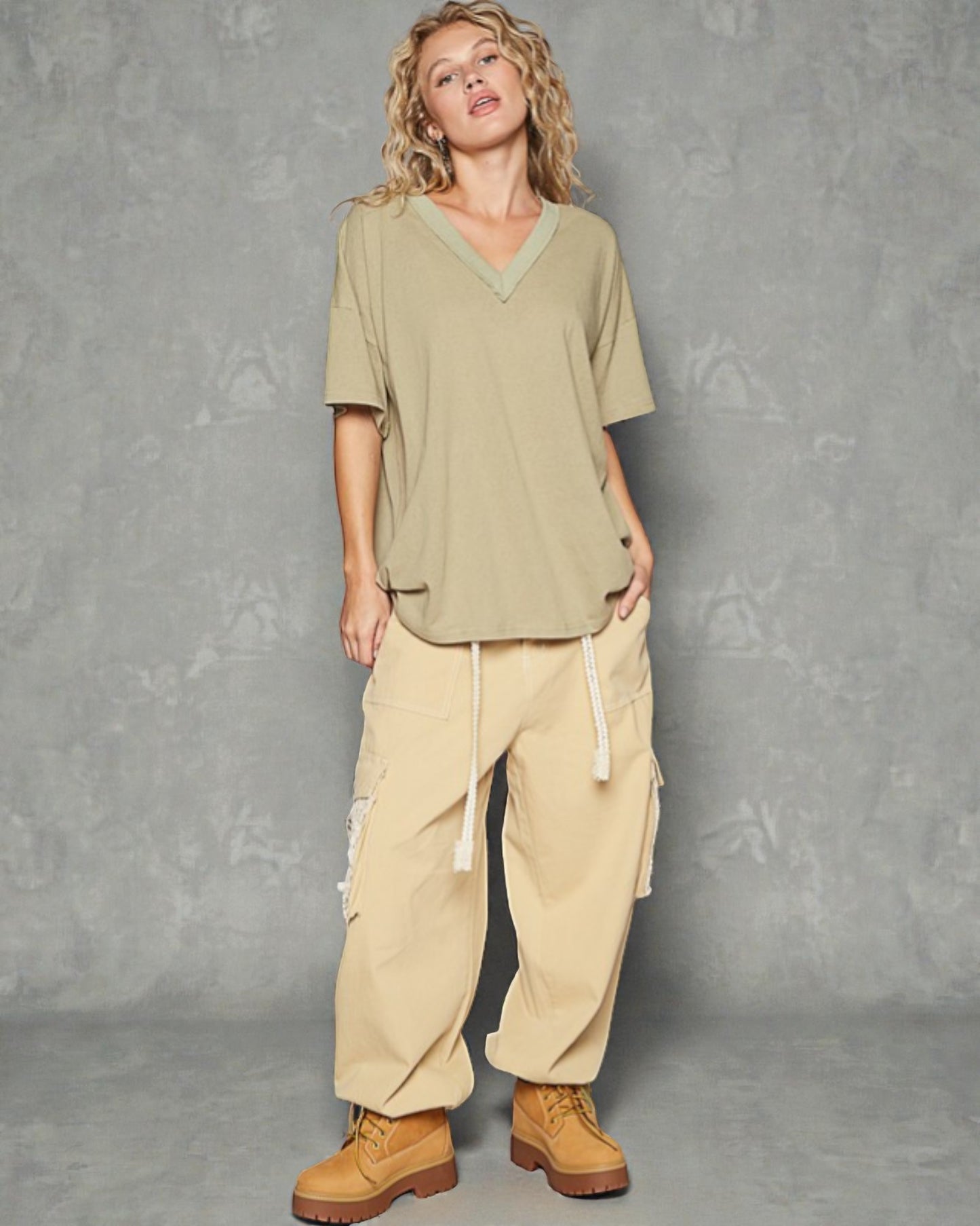 Woman wearing a green top and beige cargo pants against a gray background