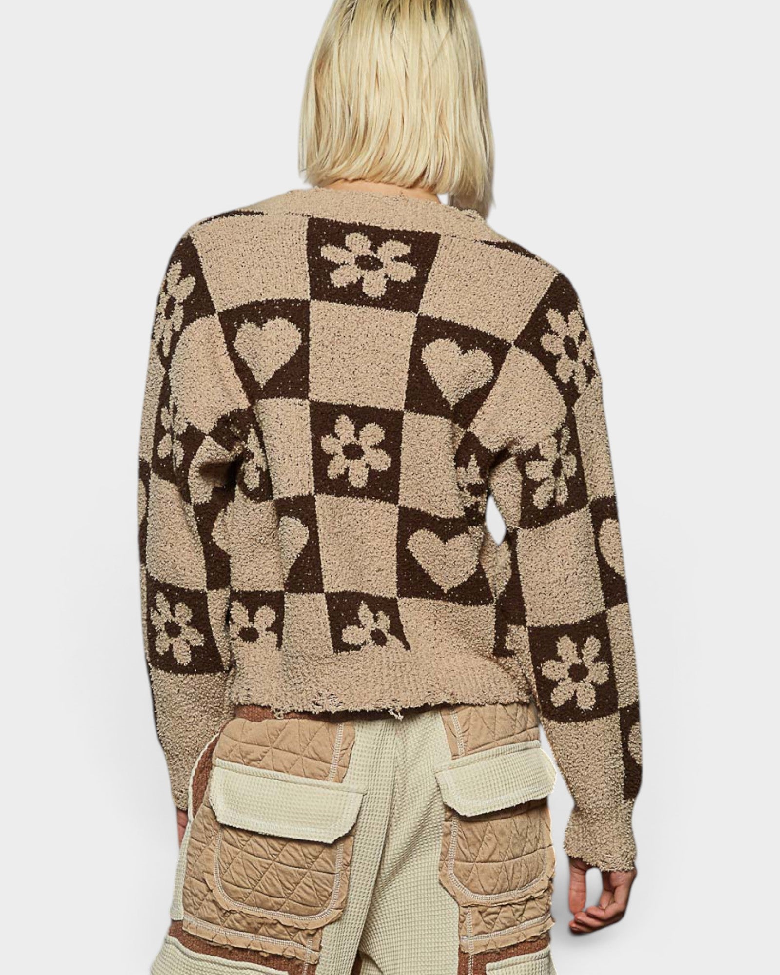 Person wearing a patterned sweater with hearts, flowers, and geometric shapes on a plain background