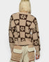 Person wearing a patterned sweater with hearts, flowers, and geometric shapes on a plain background