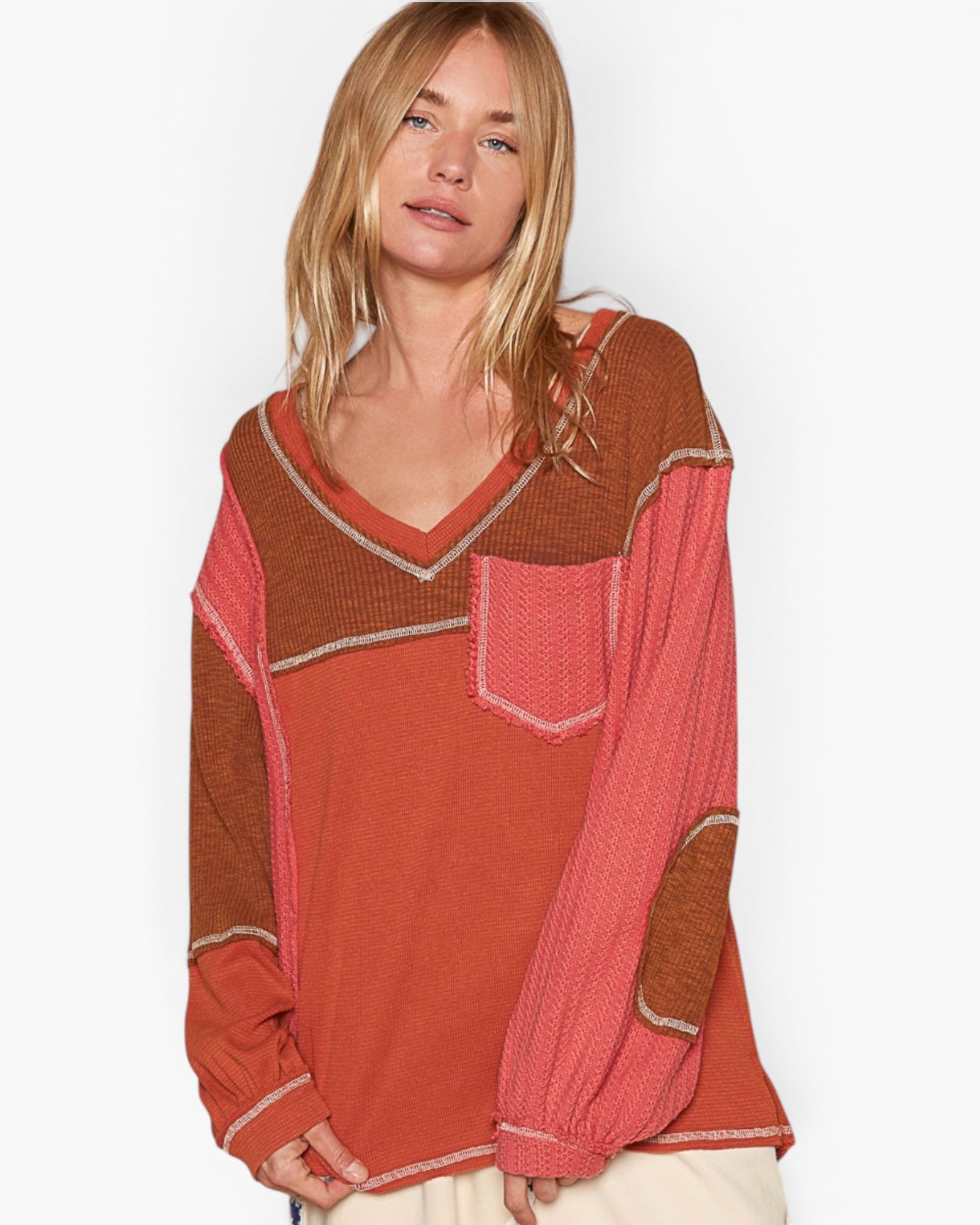 A woman wearing a long-sleeve knit sweater with a color-blocked design in rust orange, terracotta brown, and coral pink, featuring a chest pocket and contrast stitching.