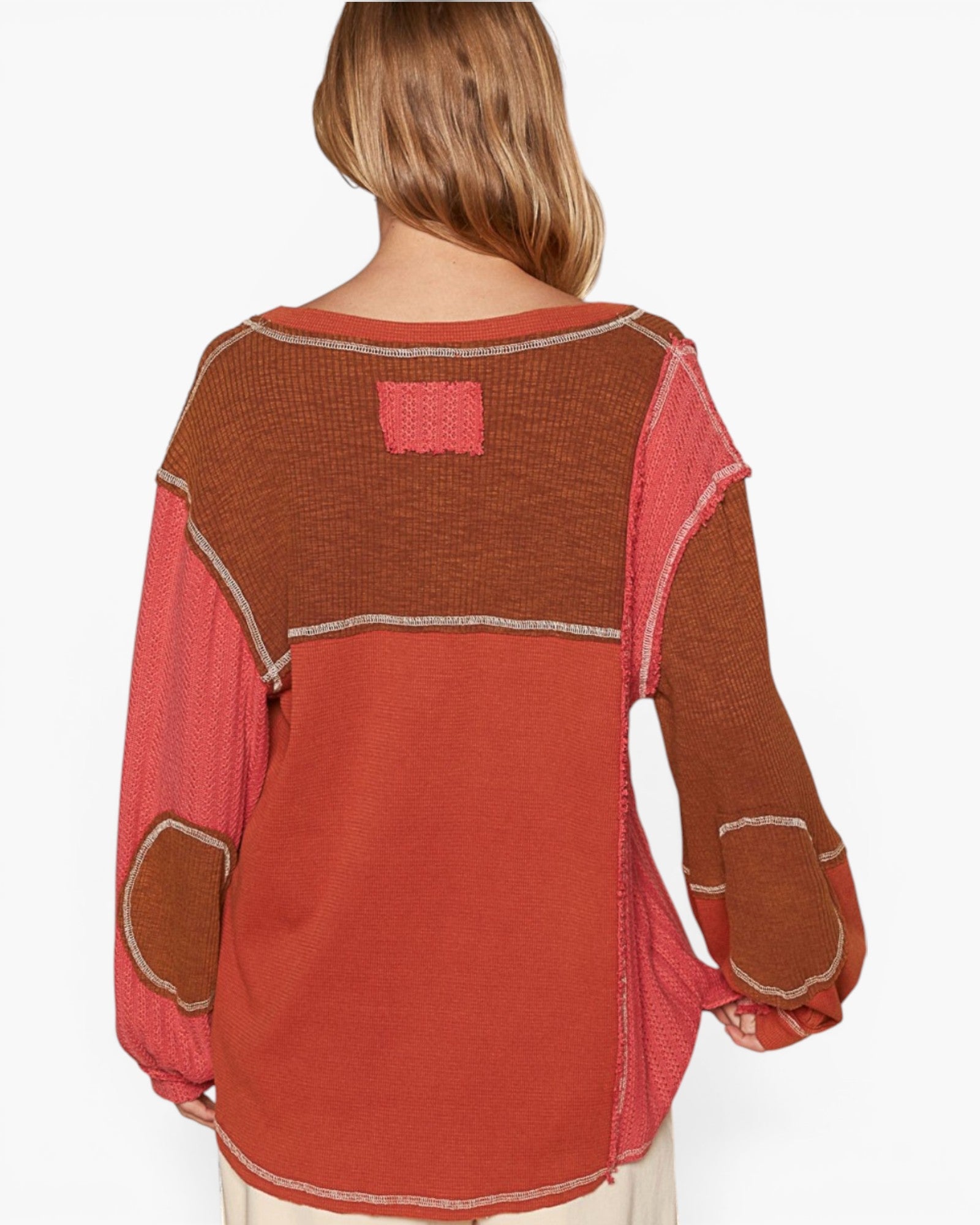 A woman shown from the back wearing a patchwork knit sweater with rust orange, terracotta red, and brown sections separated by light beige contrast stitching.