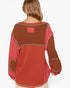 A woman shown from the back wearing a patchwork knit sweater with rust orange, terracotta red, and brown sections separated by light beige contrast stitching.