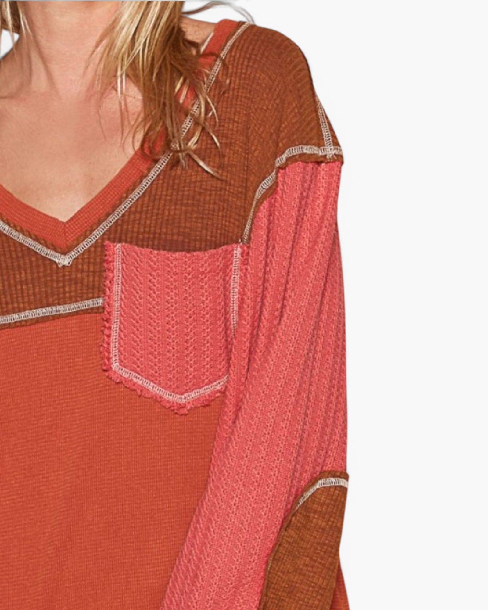 Close-up of a woman wearing a textured knit top with a color-blocked design in rust brown, coral pink, and terracotta orange, featuring a chest pocket with a contrasting pink knit panel and thin metallic trim.