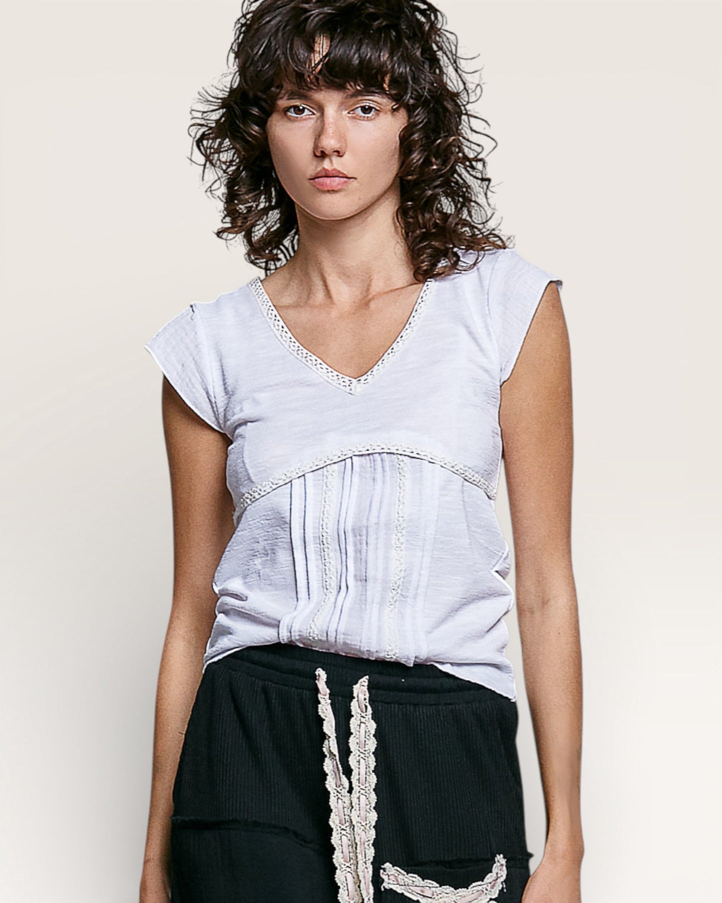 Woman wearing a light gray top with lace details on a plain background