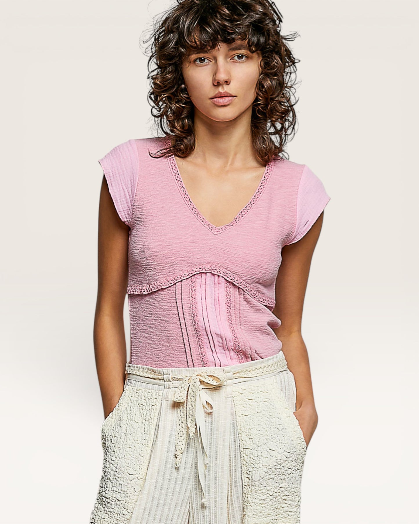 Woman wearing a pink top and white pants against a plain background